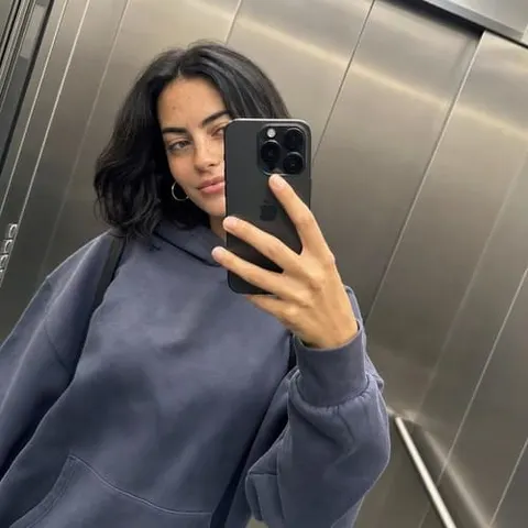 Virtual influencer taking an elevator mirror selfie in an oversized blue hoodie, with short dark hair and a casual streetwear look